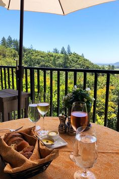 two glasses of wine are sitting on a table with food and an umbrella over it