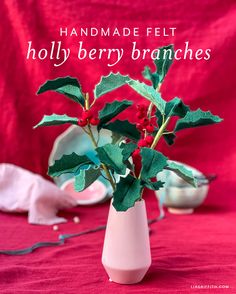 holly branches in a white vase on a red tablecloth with the words handmade felt holly berry branches