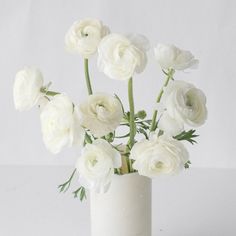 white flowers are in a vase on a table top, against a plain background that looks like something out of space