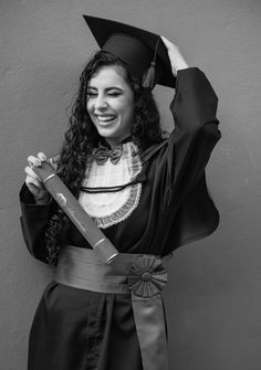 a woman wearing a graduation gown and holding a large knife in her right hand while standing next to a wall