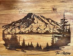 a wooden cutting board with an image of a mountain and pine trees on the side