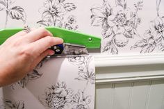 a person cutting paper with a green scissor on the side of a wall