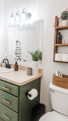 a white toilet sitting next to a green cabinet in a bathroom under a light fixture