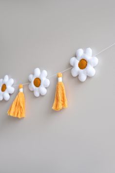 some white flowers and yellow tassels are hanging on a line that is attached to the wall