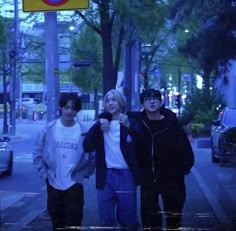 three young men walking down the street in front of a bus stop sign at night