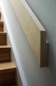 a wooden stair rail on the side of a white wall next to some wood steps