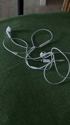 two white headphones laying on top of a green tablecloth covered floor next to a wooden chair