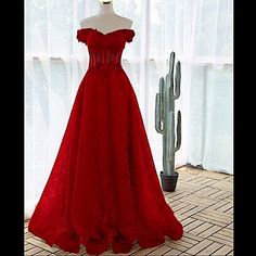 a red dress is on display in front of a cacti and curtained window