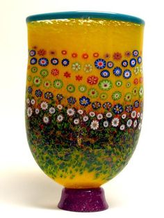 a yellow vase with flowers painted on the side and purple base, sitting against a white background