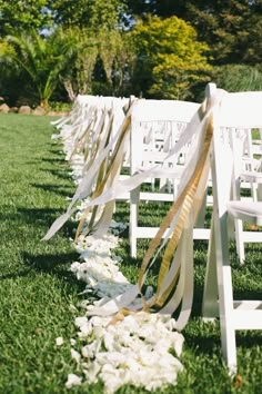 rows of white chairs lined up in the grass with ribbons tied to them and flowers on the ground