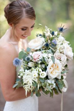 a bride holding a bouquet of white and blue flowers with greenery in her hands