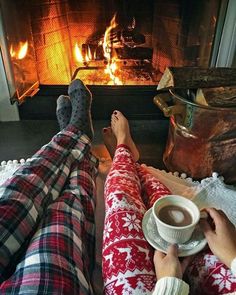 two people sitting in front of a fireplace with their feet up on the coffee cup