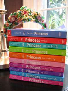 a stack of princess books sitting on top of a wooden table next to a window