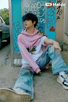 a young man sitting on the ground in front of a wall with graffiti written on it