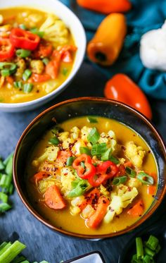 two bowls filled with soup and vegetables on top of a table