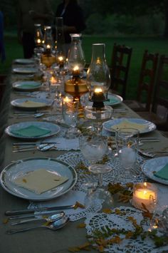 a long table is set with plates and candles for an outdoor dinner party in the evening