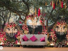 a white couch sitting under a chandelier next to a lush green forest filled with flowers