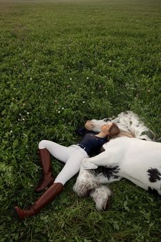 a woman laying on the ground next to a white and black dog in a field