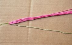 a piece of pink yarn sitting on top of a cardboard box next to a string