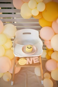 a white chair with a yellow smiley face on it and some balloons in the background