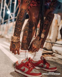 a man with tattoos on his legs and feet standing next to a pair of red sneakers