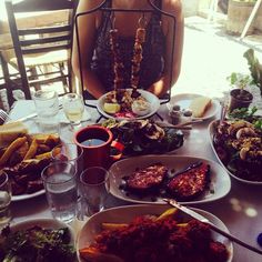 a woman sitting at a table covered in plates and bowls filled with different types of food