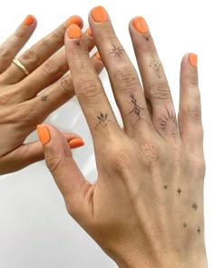 two hands with orange nail polish holding each other's fingers and pointing to the sky