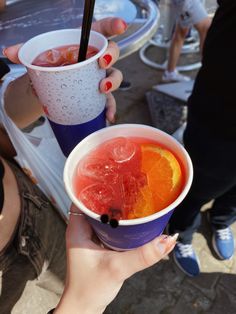 two people holding up cups with drinks in them and one has an orange slice on the rim