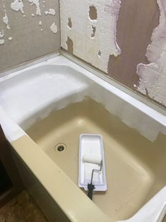 a bathtub with a brush in it and some paint on the wall behind it