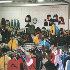 a large group of people in a room with clothes on racks and shirts hanging up