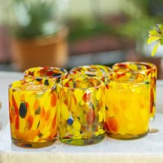 four colorful glasses sitting on top of a table next to a potted plant in the background