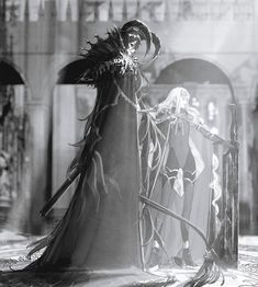 a black and white photo of a woman dressed as a witch in front of a castle