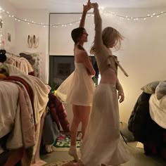 two women are dancing in a bedroom with lights strung above the bed and on the wall