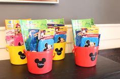 several buckets filled with mickey mouse books on a table in front of a wall