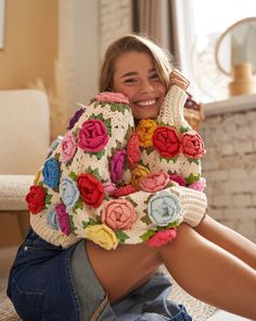 a woman sitting on the floor with her legs crossed wearing a colorful knitted sweater