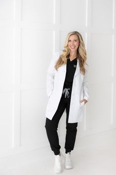 a woman standing in front of a white wall wearing black sweatpants and a white jacket