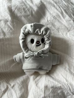 a stuffed animal in a hoodie on top of a white bed sheet with striped sheets