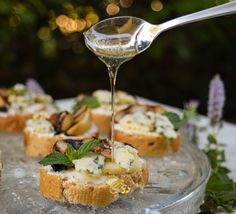 a spoon drizzling cheese onto bread with herbs