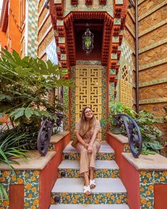 a woman sitting on the steps in front of a building with colorful tiles and plants