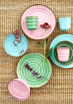 colorful plates and cups are arranged on a woven tablecloth, with flowers in the center