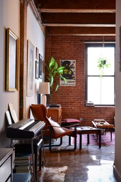 a living room filled with furniture and a piano in front of a large brick wall