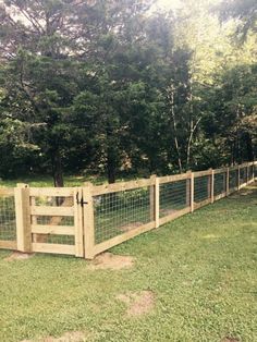 a wooden fence in the middle of a grassy area with trees and bushes behind it