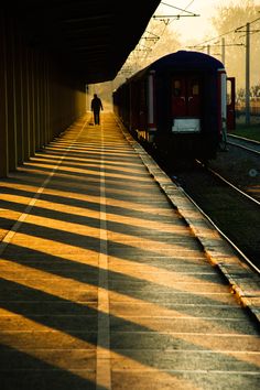 a person is walking down the train tracks in the evening sun, with their shadow on the ground