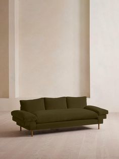 a large green couch sitting on top of a hard wood floor next to a white wall