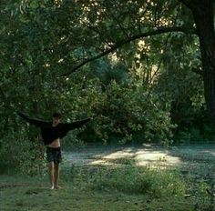 a boy standing in the grass with his arms spread out and trees behind him,