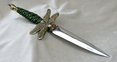 a green and gold dragonfly pendant on top of a silver knife with a beaded handle