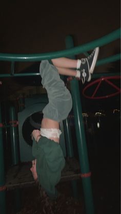 a young boy is doing a handstand on a green playground structure at night