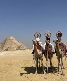 three people are riding on camels in front of the pyramids