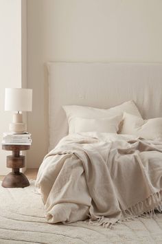 a bed with white linens and pillows in a bedroom next to a lamp on the floor