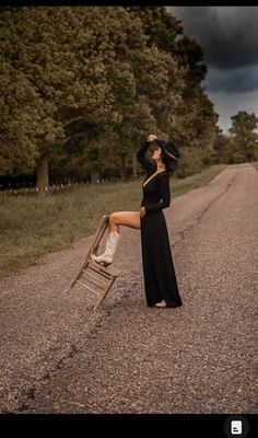 a woman in a long black dress leaning on a ladder